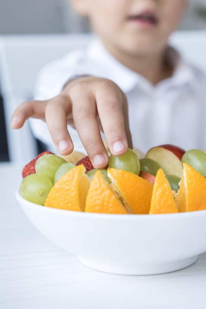 child digging into a fruit bowl