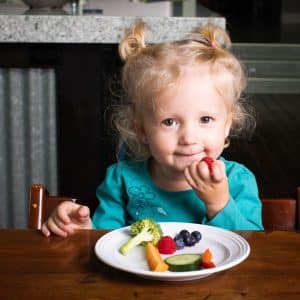 Young picky eater at the table with a plate of fruit and vegetables